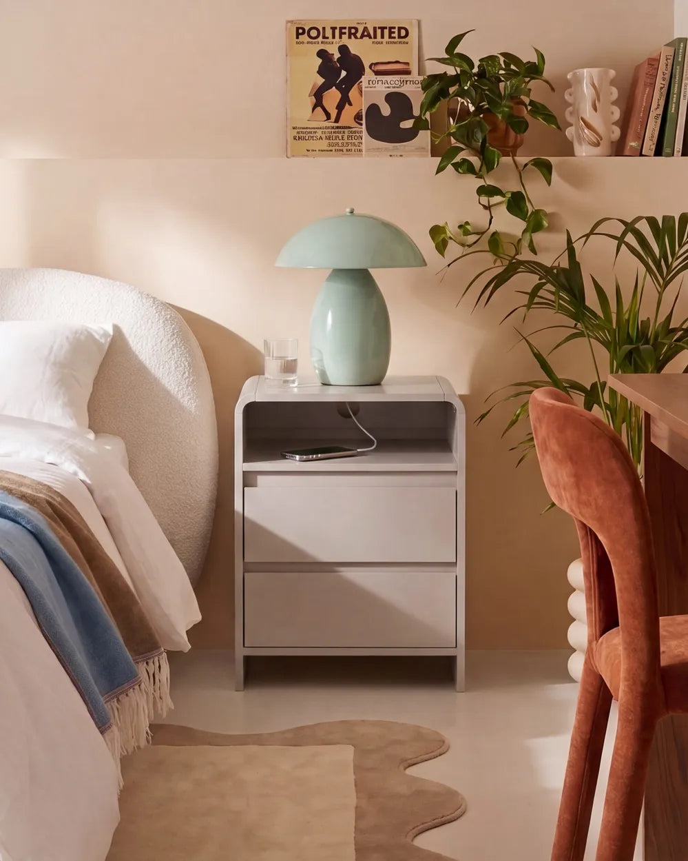 A modern light gray two-drawer nightstand in a styled bedroom setting, featuring a mint green dome lamp on top, next to a bed and a wooden chair.