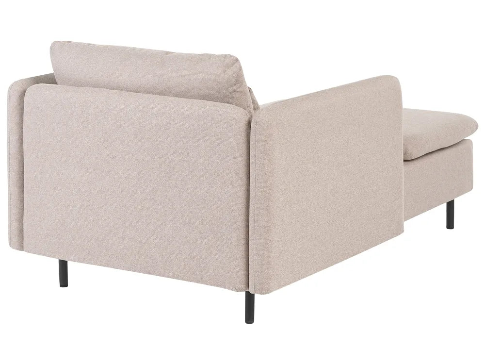 A light beige upholstered sectional sofa shown from a three-quarter rear angle, featuring a high back cushion, wide armrests, and slim black legs on a plain white background.