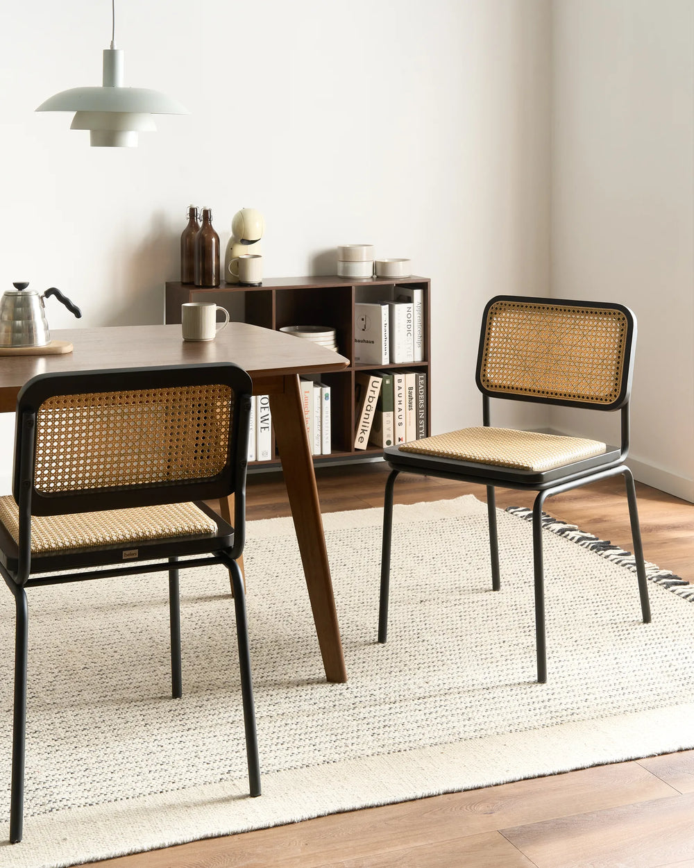 Dining area with wooden table and wicker chairs on a light rug.