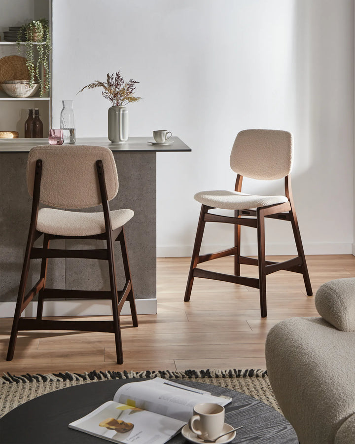 Two bar stools with wooden legs and beige cushioned seats in a modern kitchen setting.