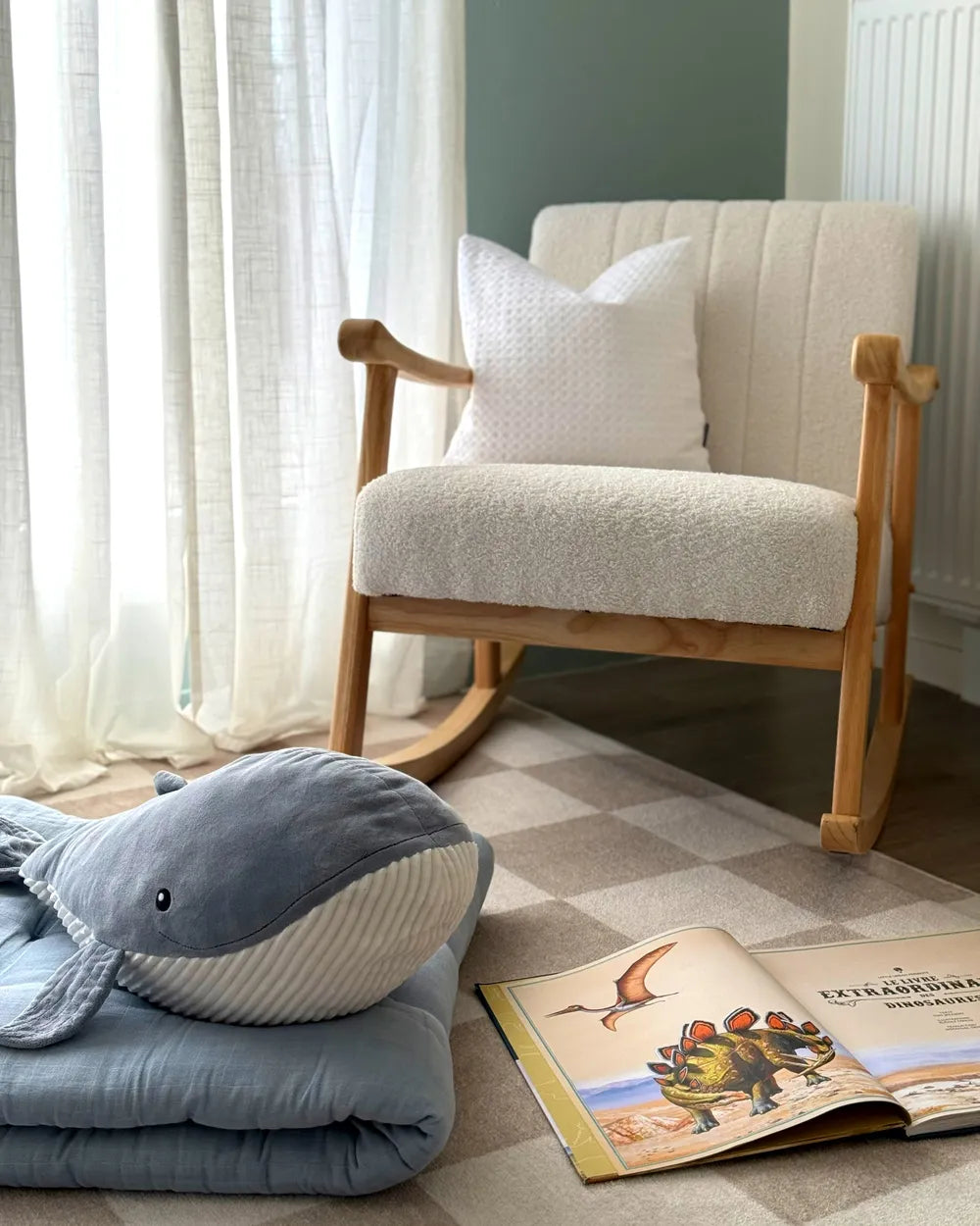 Rocking chair with a pillow and a plush shark toy on a checkered floor, next to an open book.