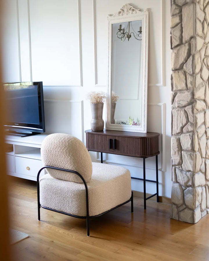 Beige armchair in a living room with a stone wall and mirror.