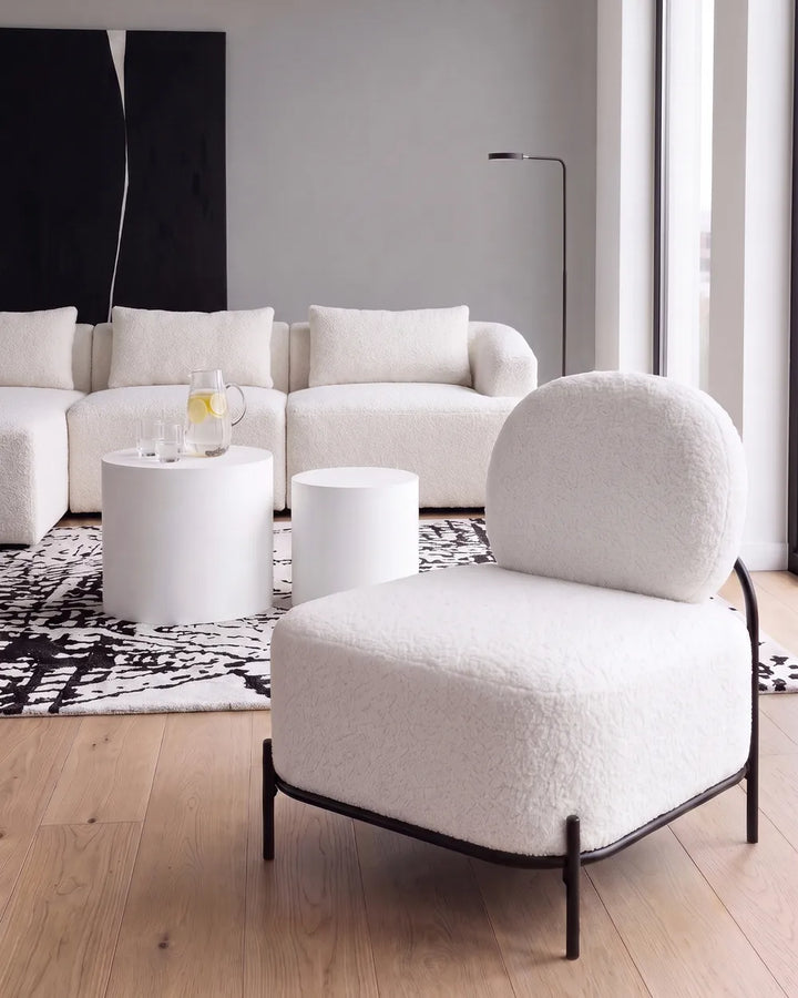 A modern white bouclé lounge chair with a black metal frame in a bright, contemporary living room setting.