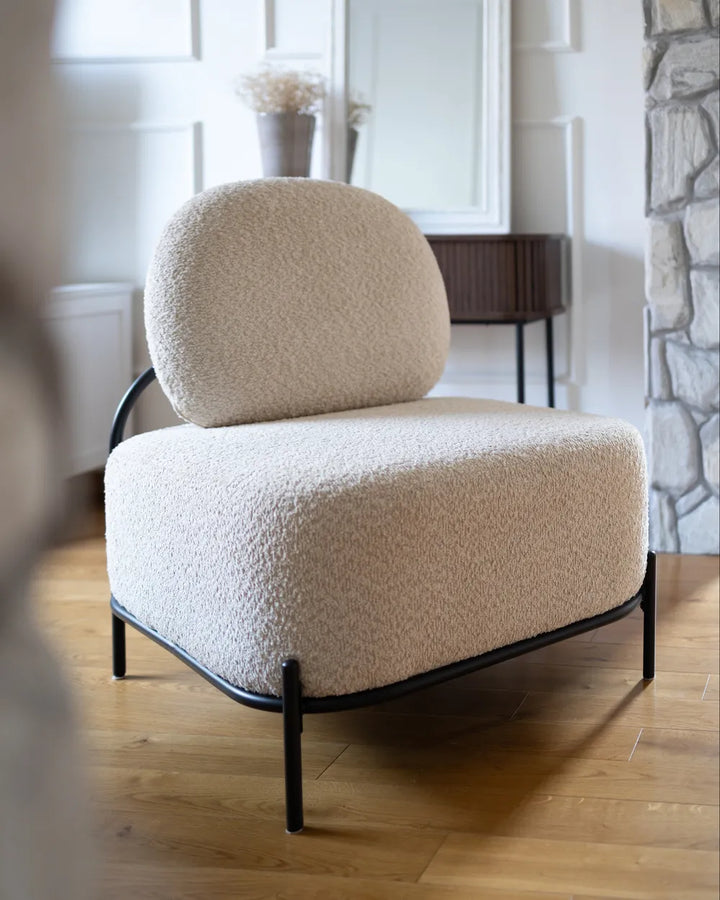 Beige armchair with black metal frame in a room with wooden floor and stone wall.