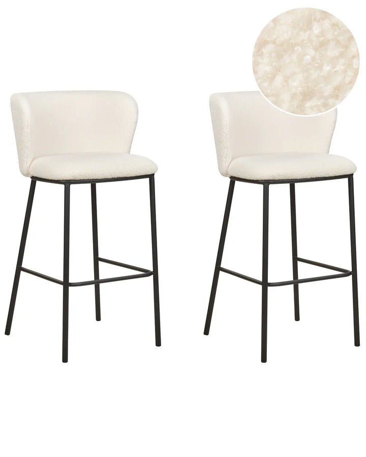 Two modern bar stools with cream upholstered seats and curved backs on black metal legs, shown on a white background with a circular fabric close-up inset.