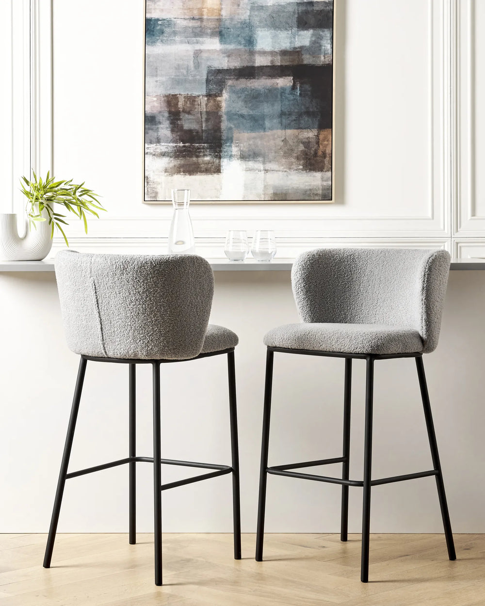 Two gray bar stools with black legs in a kitchen setting with abstract art on the wall.