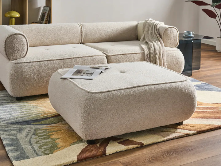 Beige sectional sofa with ottoman on a patterned rug in a living room setting.