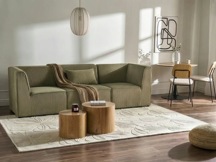 Modern living room with a green sectional sofa, wooden coffee tables, and decorative items.