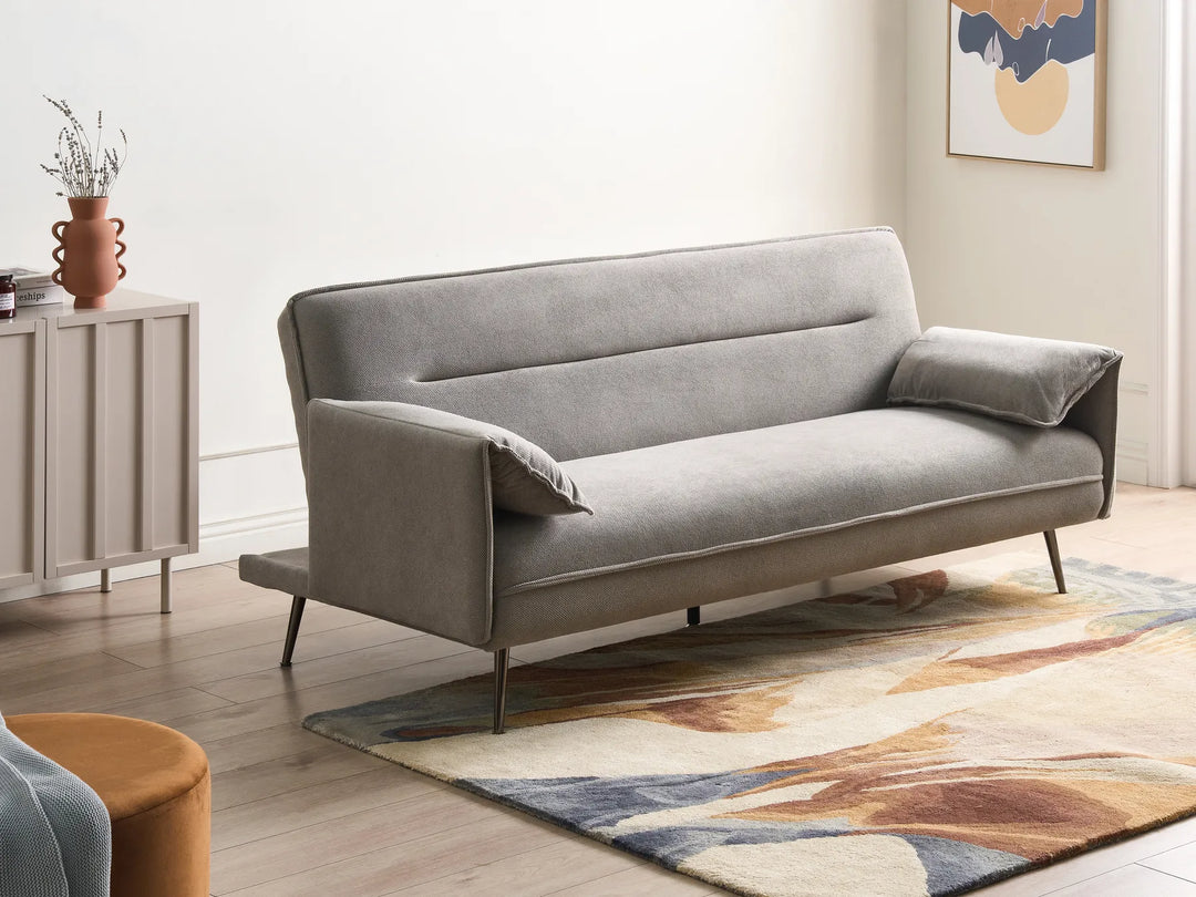 Gray sofa in a living room setting with a rug and side table.