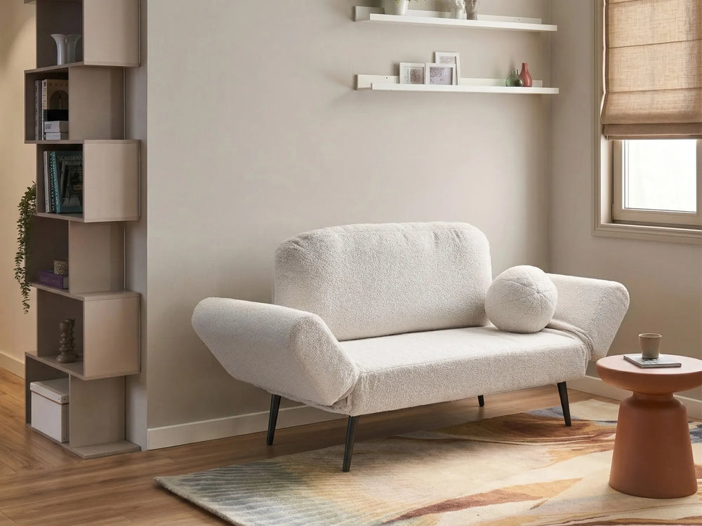 A modern two-seater sofa upholstered in a textured cream bouclé fabric, styled in a minimalist living room with a matching round throw pillow, a terracotta side table, and a geometric patterned rug.