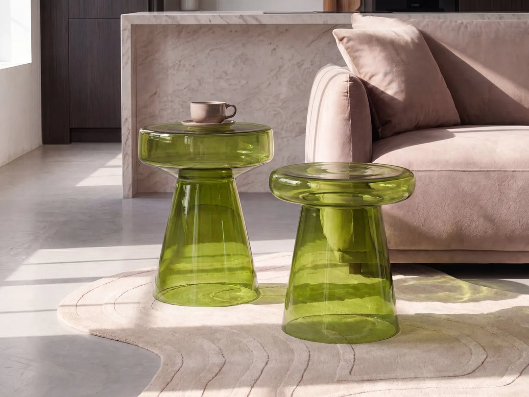 Two translucent olive green glass side tables with a flared pedestal base, styled in a modern living room next to a beige sofa.