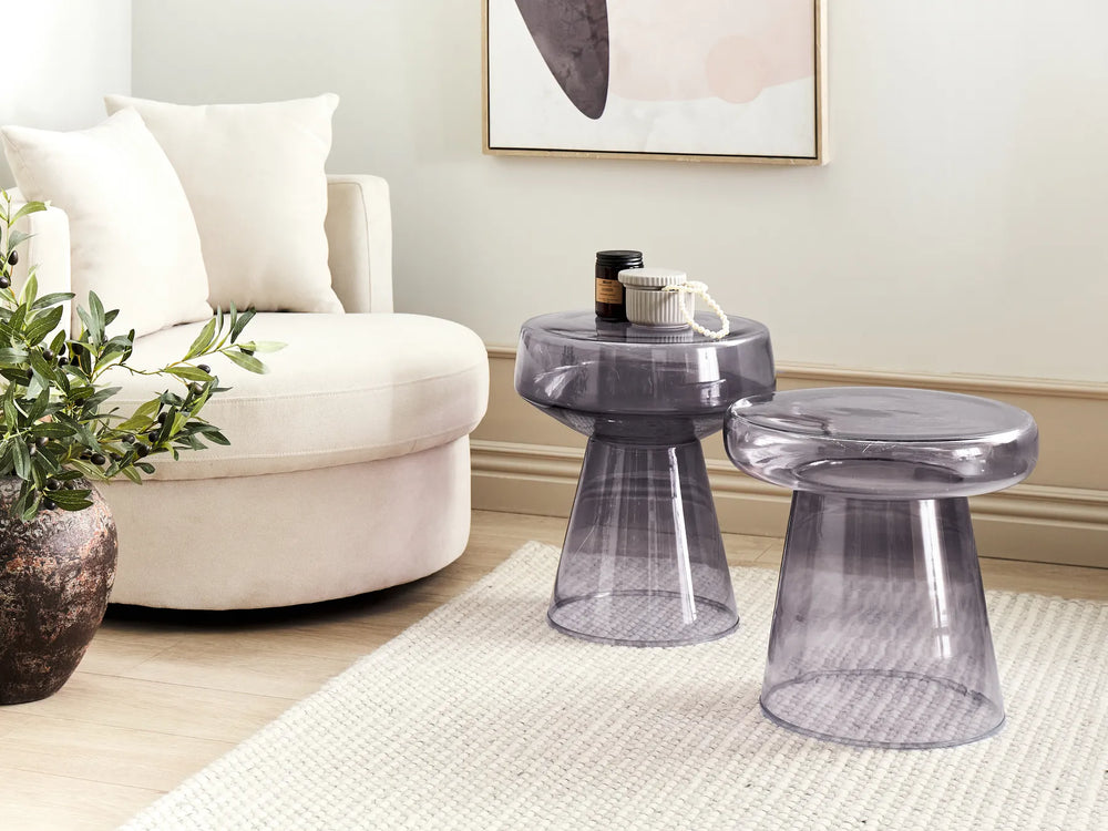 Transparent side table and stool in a living room setting with a white armchair and decorative elements.