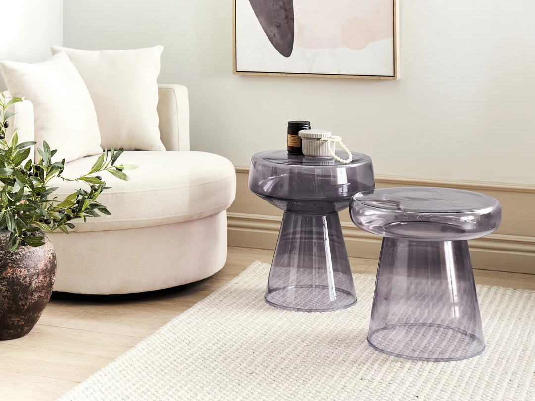 Transparent side table and stool in a living room setting with a white armchair and decorative elements.