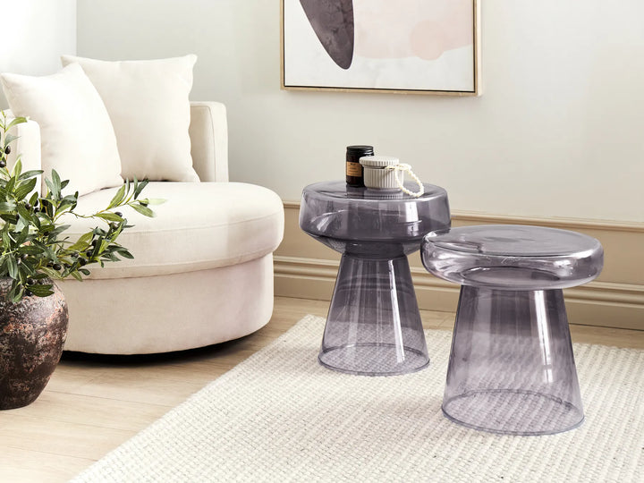 Transparent side table and stool in a living room setting with a white armchair and decorative elements.