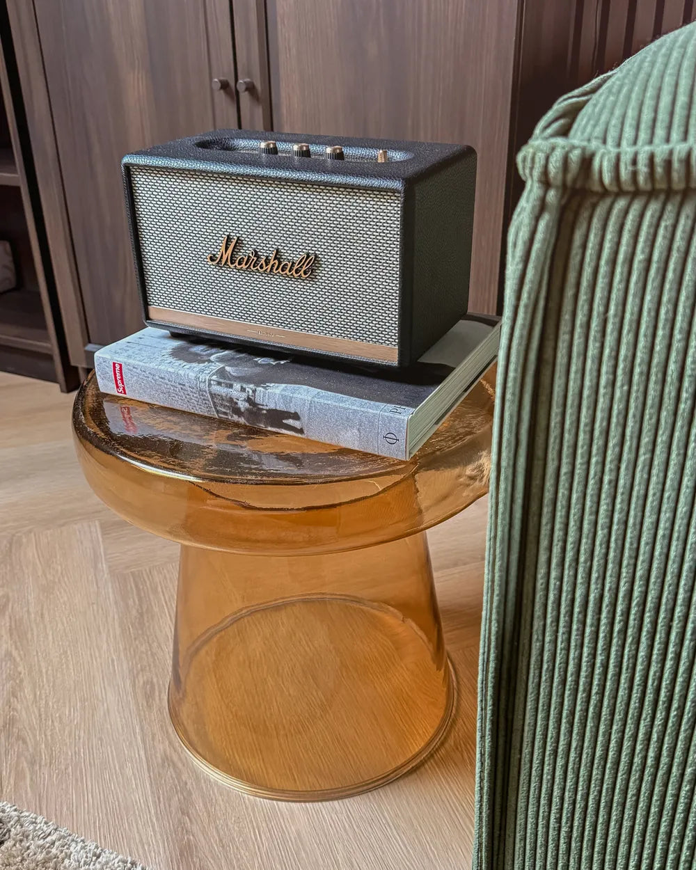 Marshall speaker on a glass side table with a book underneath, in a room setting.