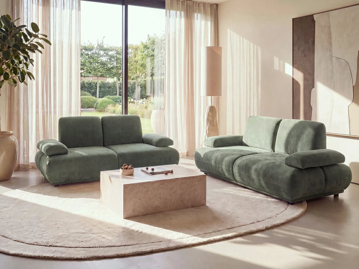 A modern living room featuring a sage green modular sofa set, including a two-seater loveseat and a three-seater sofa, arranged around a light stone coffee table on a round beige rug.