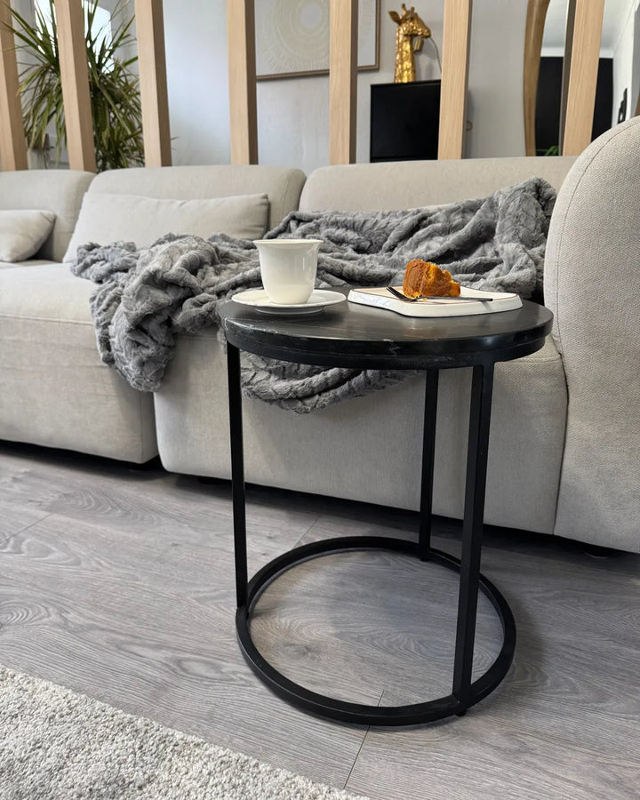Small round black side table with a cup and snack in a living room setting.