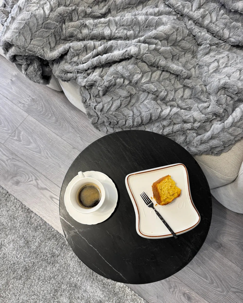 Small round table with a plate of toast and coffee under a gray blanket.