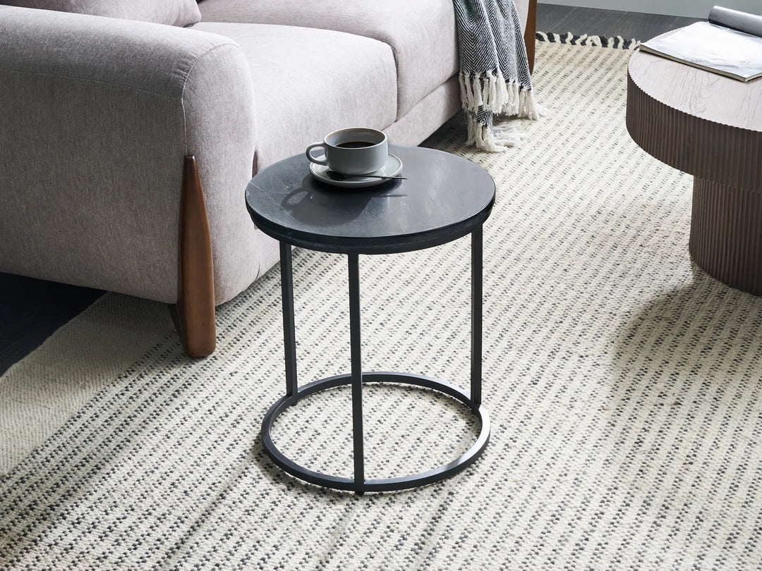 Small round black table with a cup on a patterned rug in a living room.