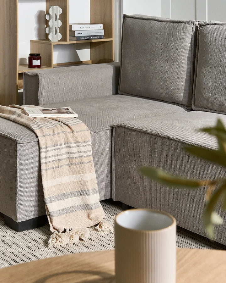 A modern gray fabric sectional sofa in a styled living room setting, featuring a beige and gray striped throw blanket draped over the chaise lounge.