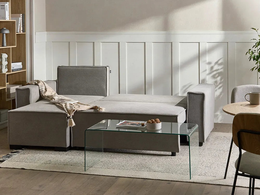 A modern gray fabric sectional sofa with a chaise lounge, styled in a bright living room with a glass coffee table, textured rug, and wood-paneled wall.