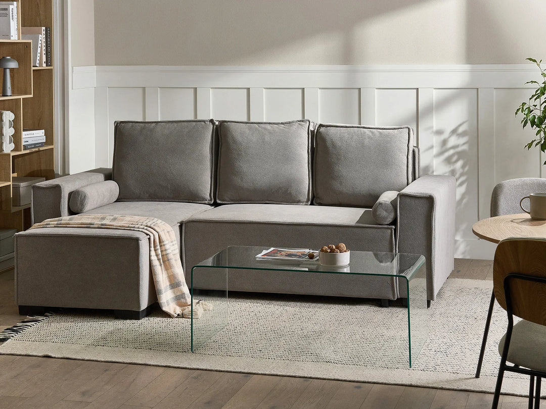 Gray sectional sofa in a living room with a glass coffee table and decorative items.