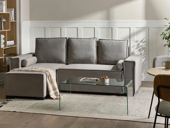 Gray sectional sofa in a living room with a glass coffee table and decorative items.
