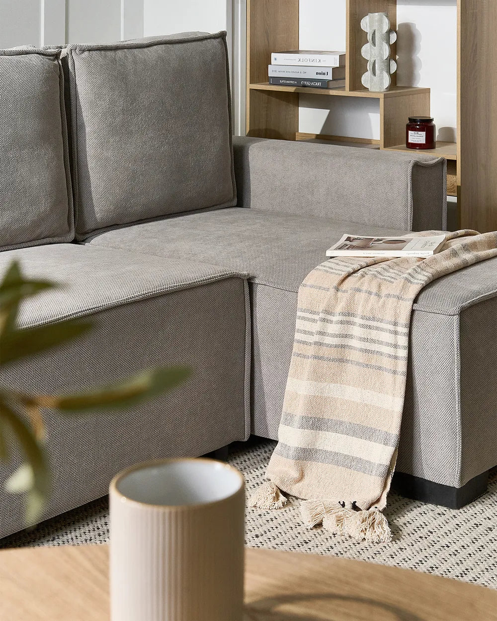 A modern gray fabric sectional sofa in a styled living room setting, featuring a striped beige and gray throw blanket draped over the armrest.