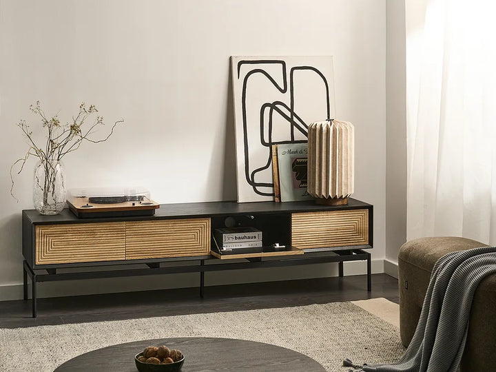 A modern black and natural wood TV stand in a styled living room setting, decorated with a lamp, framed art, and a record player.