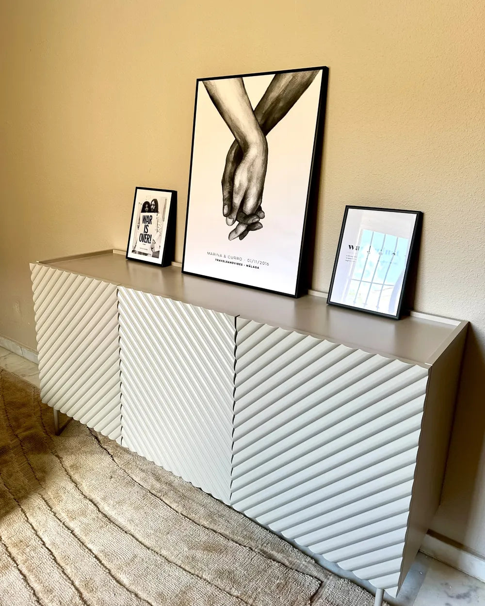 A modern sideboard or credenza with a textured chevron pattern in light gray and white, styled in a room setting with framed art on top.