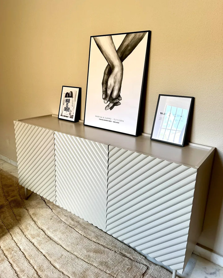 A modern sideboard or credenza with a textured chevron pattern in light gray and white, styled in a room setting with framed art on top.