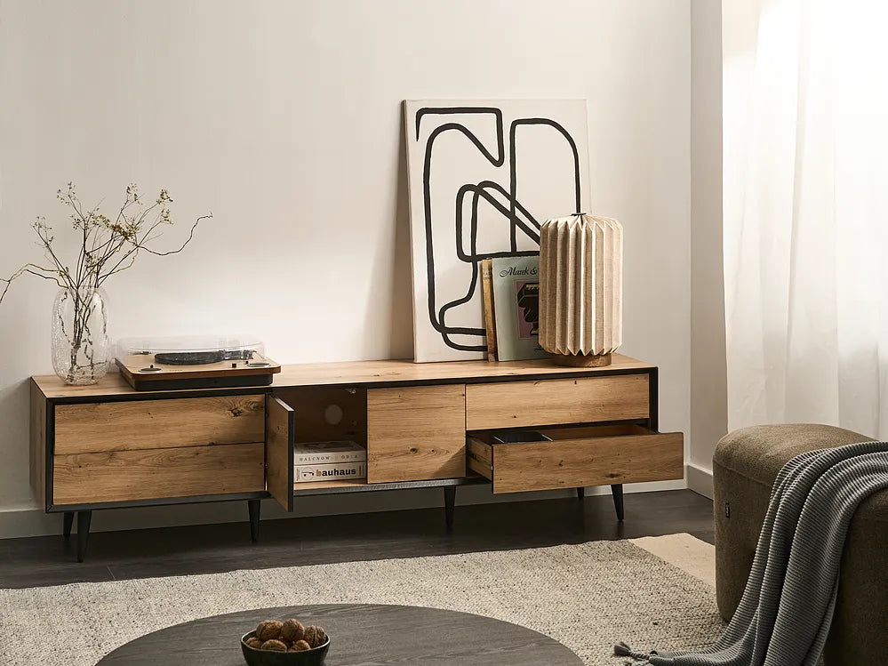 A modern wooden media console with black metal legs and open shelving, styled in a minimalist living room setting with a lamp, framed art, and a record player.