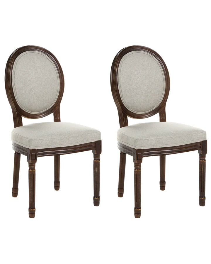 Two matching wooden dining chairs with oval backrests upholstered in light beige fabric, shown side by side on a plain white background.