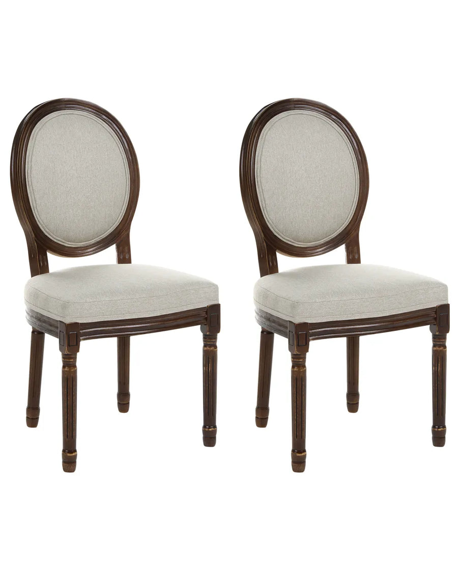 Two matching wooden dining chairs with oval backrests upholstered in light beige fabric, shown side by side on a plain white background.