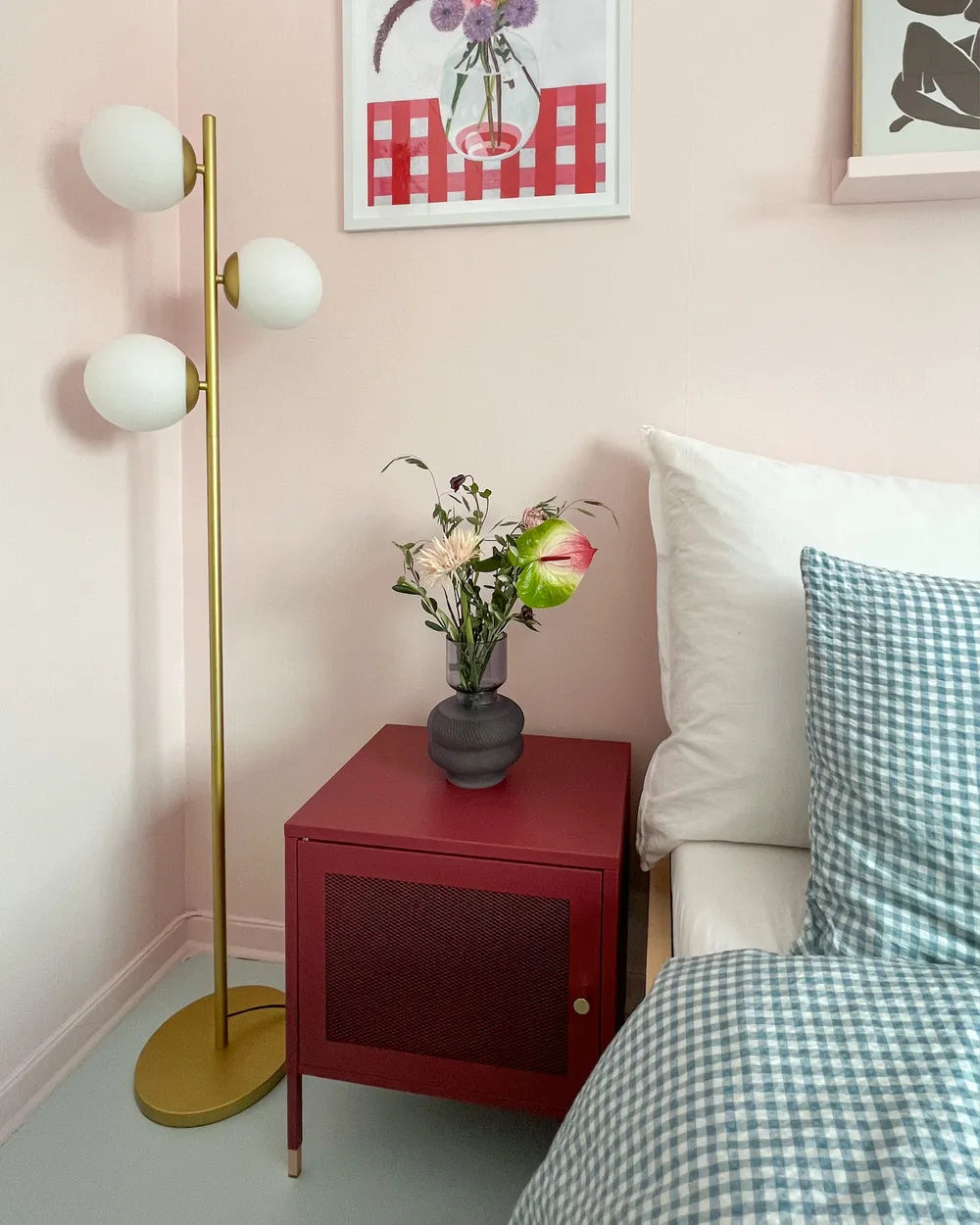 Bedroom with a red nightstand, gold floor lamp, and floral arrangement.