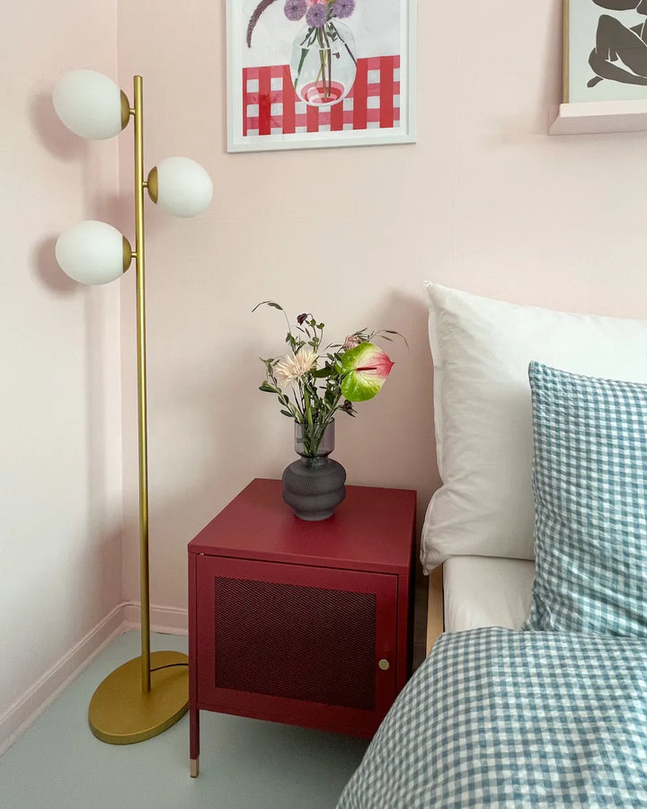 Bedroom with a red nightstand, gold floor lamp, and floral arrangement.