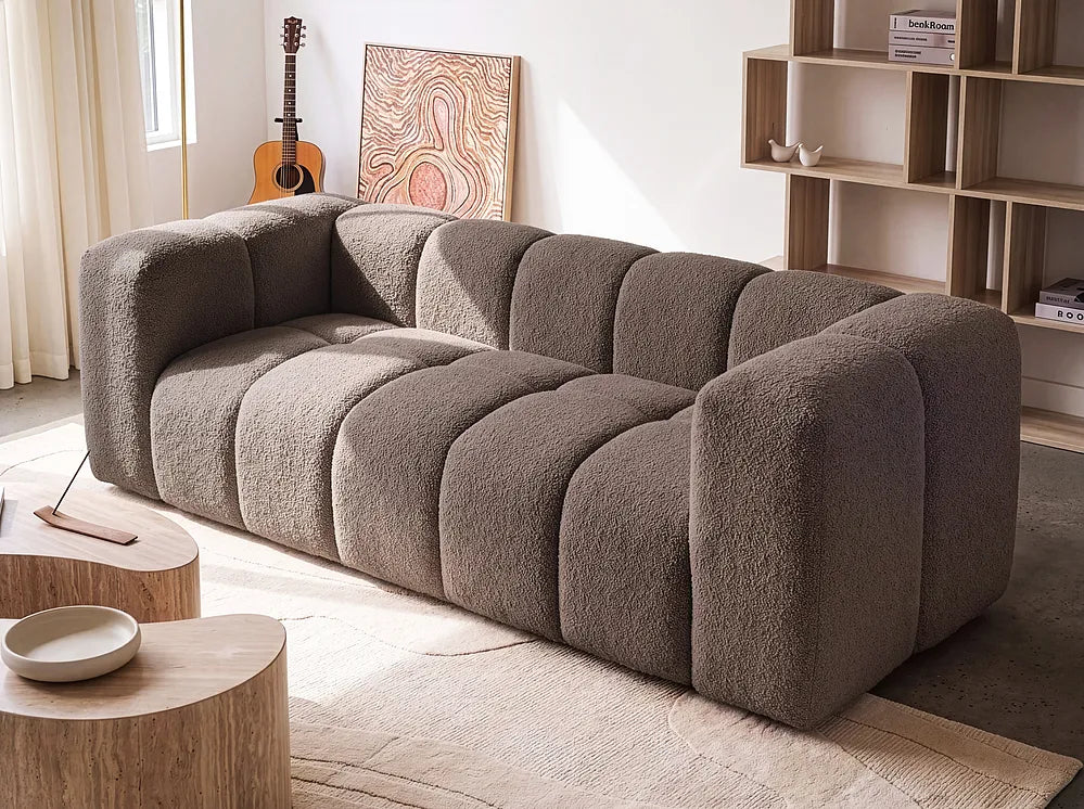 A modern modular sofa with a chunky, bubble-like segmented design upholstered in a textured taupe bouclé fabric, shown in a bright, contemporary living room setting.