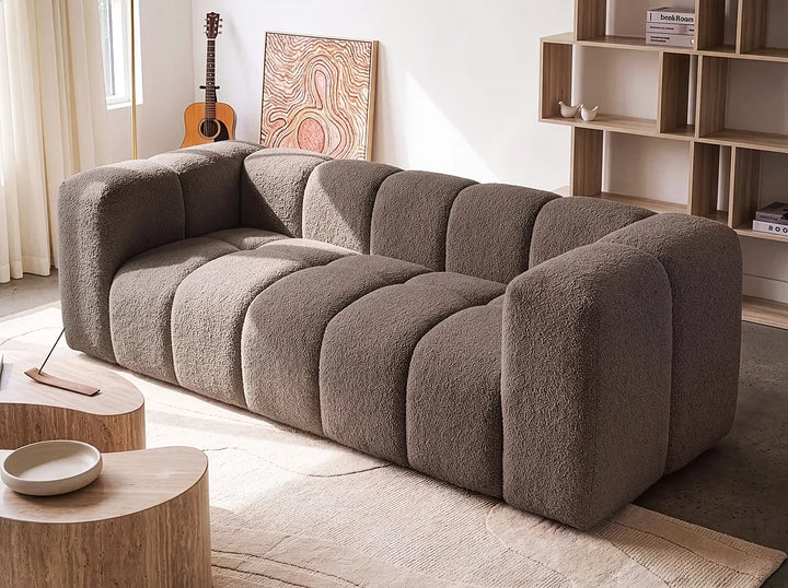 A modern modular sofa with a chunky, bubble-like segmented design upholstered in a textured taupe bouclé fabric, shown in a bright, contemporary living room setting.
