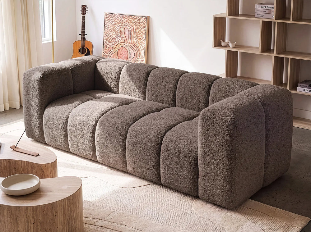 A modern modular sofa with a chunky, bubble-like segmented design upholstered in a textured taupe bouclé fabric, shown in a bright, contemporary living room setting.