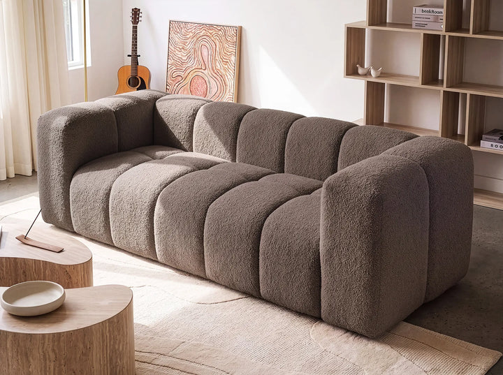 A modern modular sofa with a chunky, bubble-like segmented design upholstered in a textured taupe bouclé fabric, shown in a bright, contemporary living room setting.