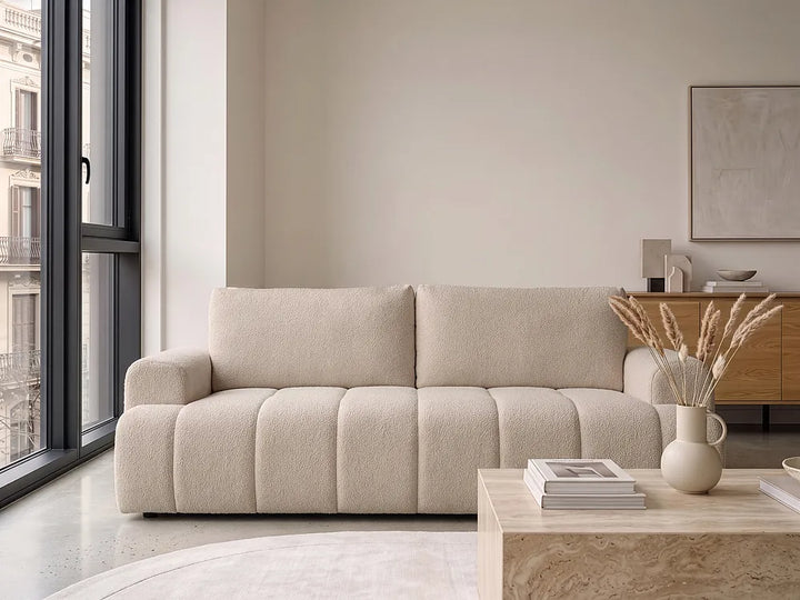 A modern beige bouclé three-seater sofa in a bright, contemporary living room.