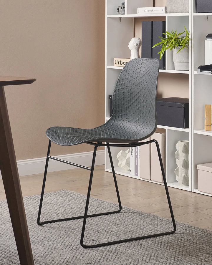Modern gray chair with black legs in a room with a bookshelf and table.