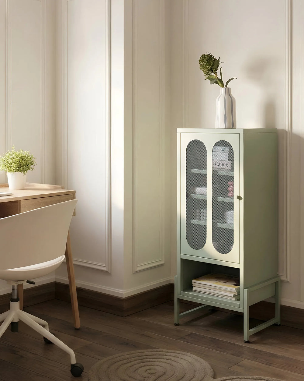 A sage green metal storage cabinet with glass doors and a lower shelf, styled in a bright home office next to a desk and chair.