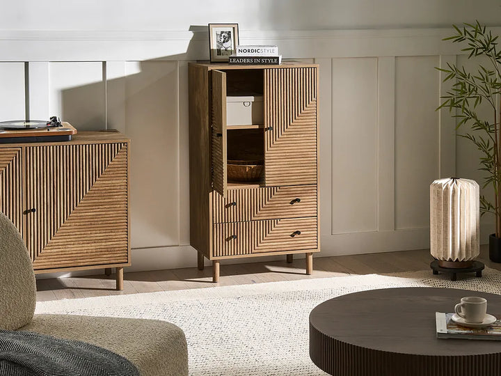 A mid-century modern wooden cabinet with a distinctive slatted geometric pattern, shown in a styled living room setting next to a matching sideboard, a round coffee table, and a potted plant.