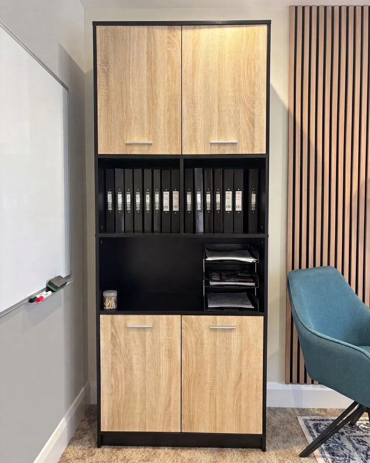 A tall black-framed office storage cabinet with light oak wood grain doors and open shelves, shown in a home office setting next to a whiteboard, wood slat wall, and teal chair.
