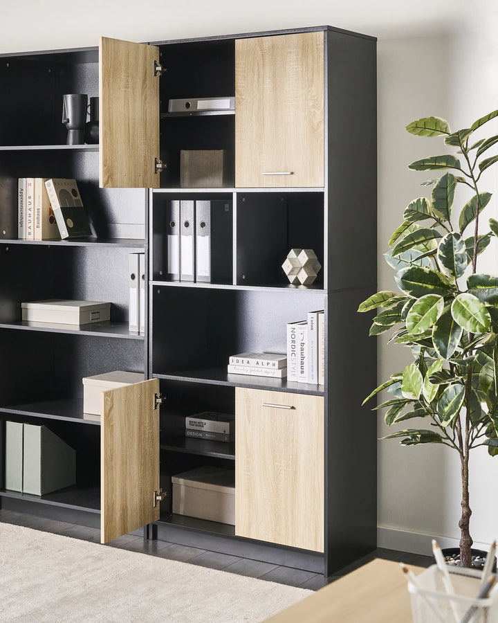 Tall black and wood bookshelf with open doors in a room with a plant.