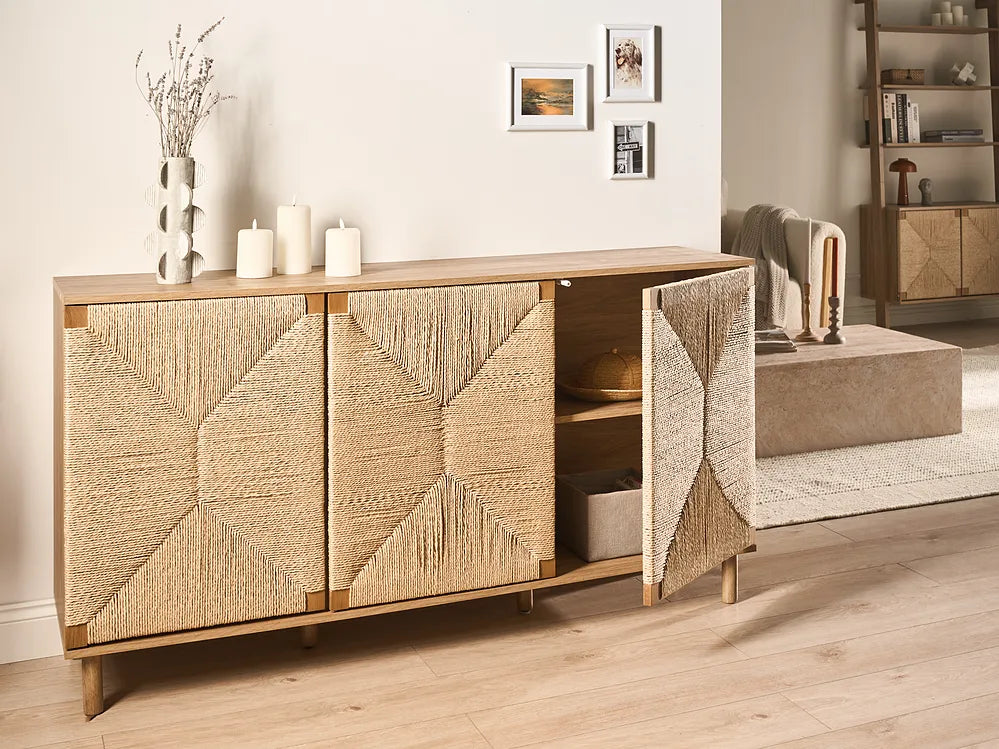 A mid-century modern wooden sideboard cabinet with woven rattan doors, shown in a styled living room setting with one door open to reveal shelves inside.