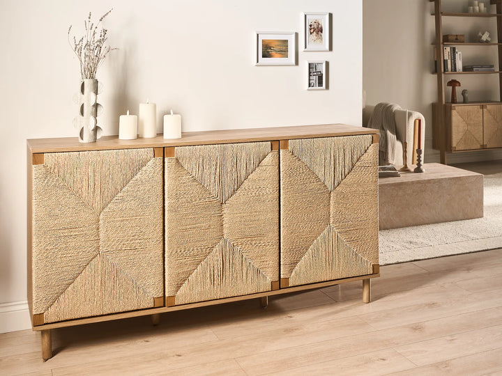 A mid-century modern sideboard cabinet with three doors featuring a geometric woven rattan pattern, finished in light natural wood with brass-toned metal frames, shown in a styled living room setting.