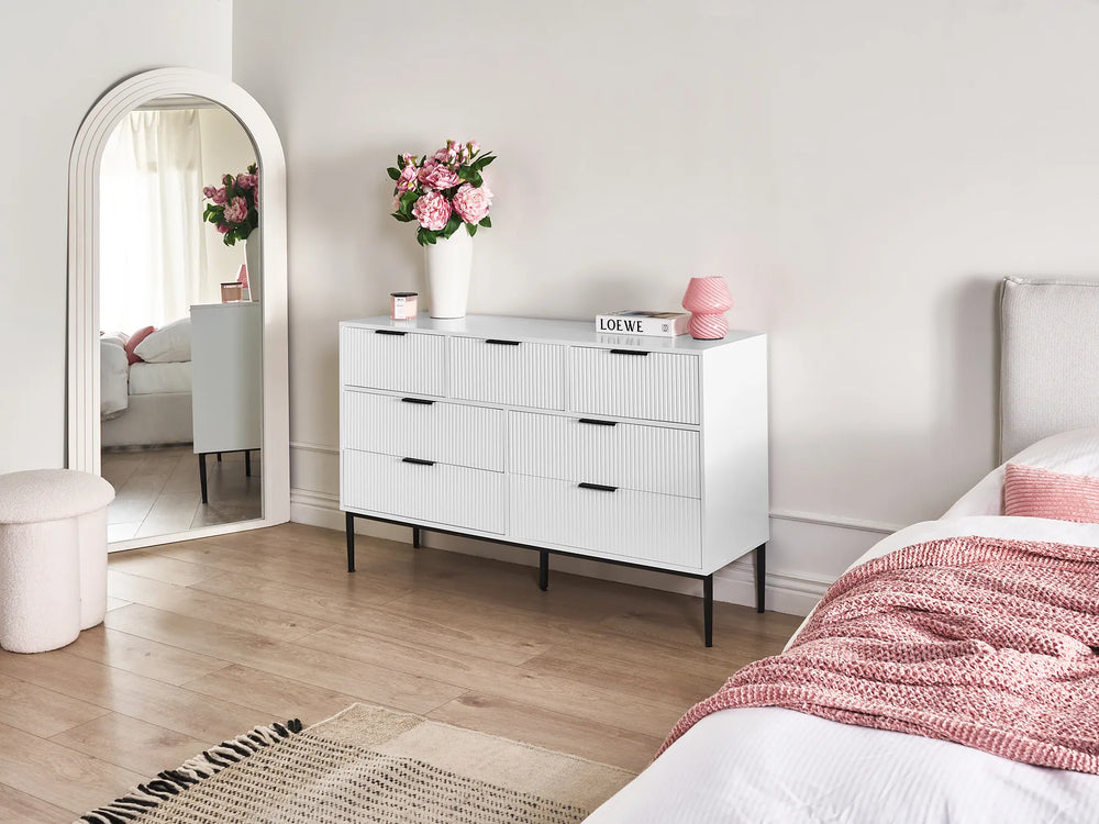Modern bedroom with a white dresser, mirror, and bed with pink bedding.