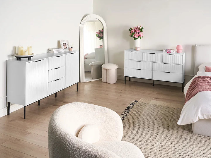 Modern bedroom with white furniture, including a dresser and mirror, and decorative elements.